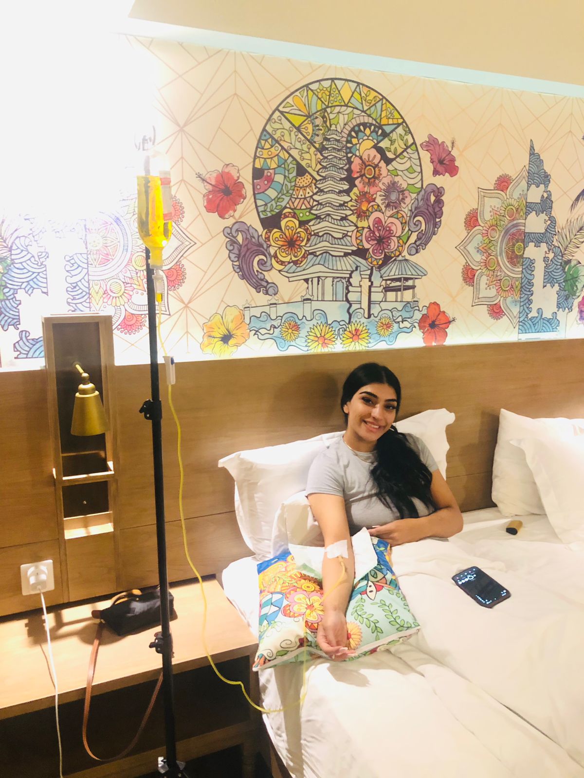 A woman receiving a mobile IV drip treatment while relaxing in a Bali hotel room.