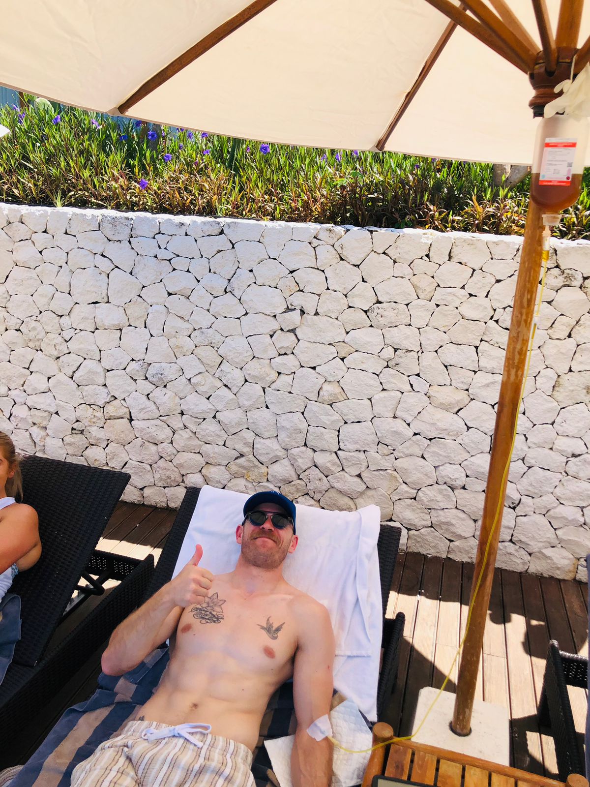 Man relaxing on a lounge chair receiving a mobile IV drip treatment outdoors in Bali.